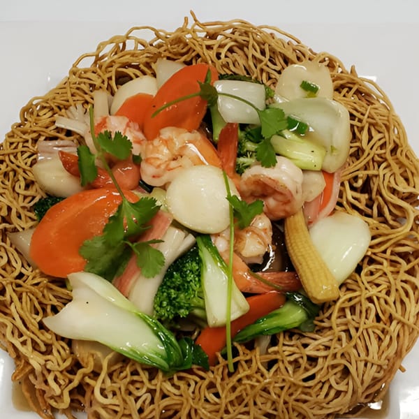 Crispy Vietnamese egg noodles topped with shrimp, scallops, and mixed vegetables on a white plate.