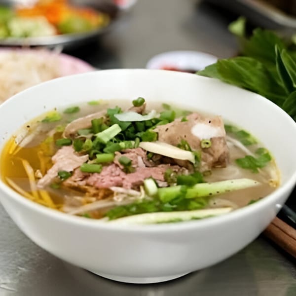 A white bowl of Pho America Vietnamese pho with meat, noodles, and green onions.