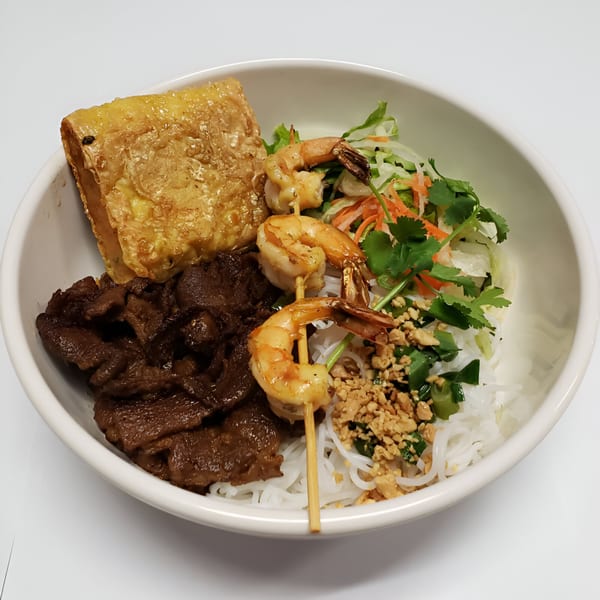 Vietnamese vermicelli bowl with grilled beef, shrimp skewers, fried spring roll, and fresh vegetables.