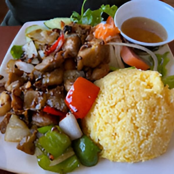 Vietnamese dish with stir-fried meat and vegetables, yellow rice, and a side of sauce.