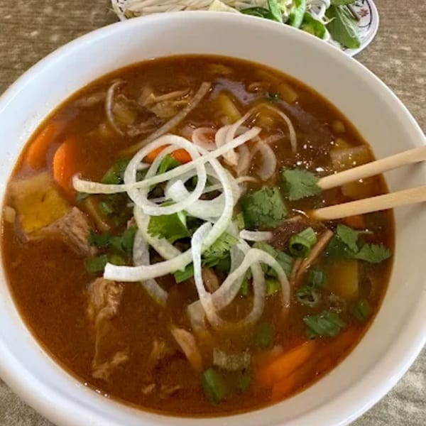 Close-up of a bowl of Vietnamese pho with beef, carrots, onions, and cilantro, with chopsticks.