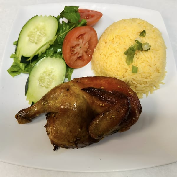 Roasted chicken with yellow rice, sliced tomatoes, cucumbers, and lettuce on a white plate.